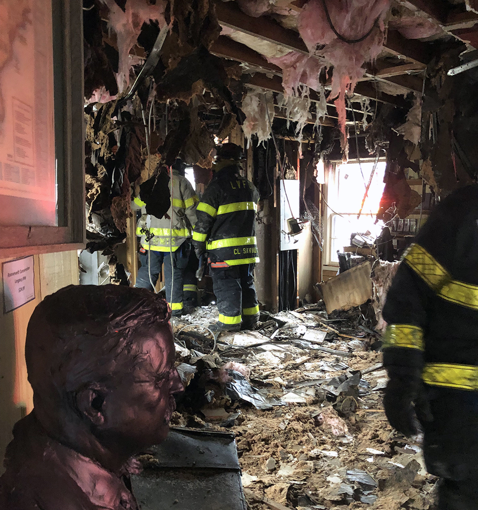 Damage from the visitor center fire. The bust of Theodore Roosevelt sits in a recently burned room with structural firefighters looking around.