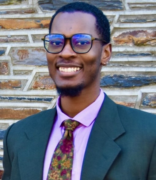 Dr. Tayzhaun Glover Headshot of a Black man wearing a green suit jacket, pink shirt and floral tie