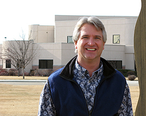 Jeff Scott stands next to a sign in front of a multi-story building.