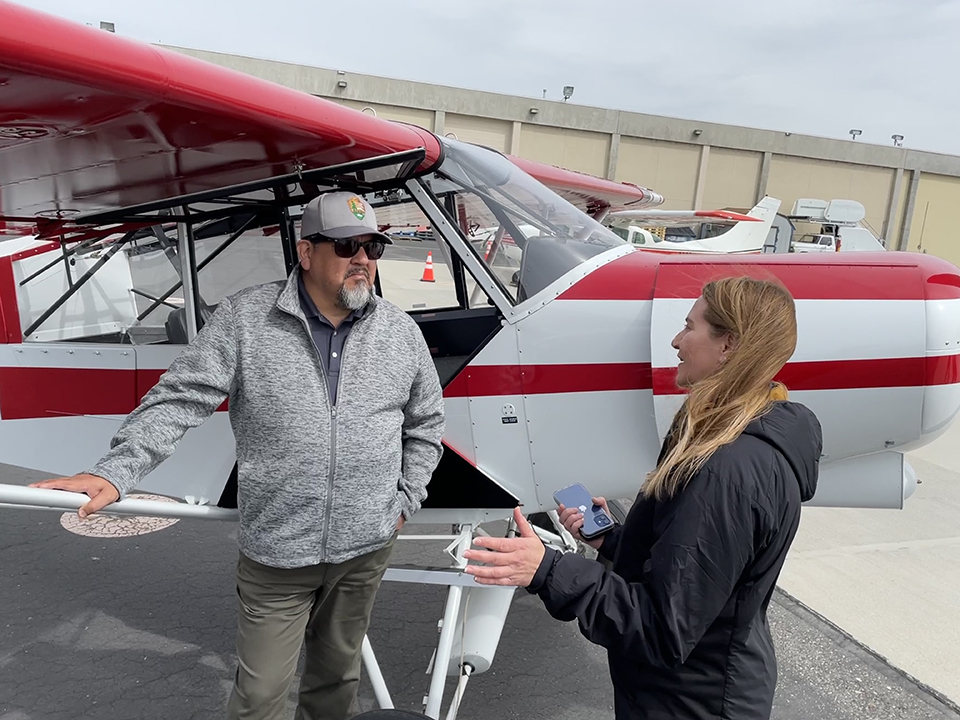 Kristin Swoboda briefs Chuck Sams about NPS aircraft. Director Sams and Kristin Swoboda stand next to a red and white airplane.