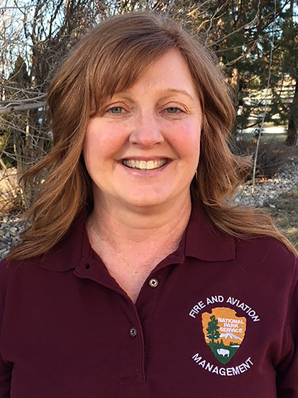 Headshot of Roberta Gorman wearing maroon polo shirt with logo standing in front of wooded area.