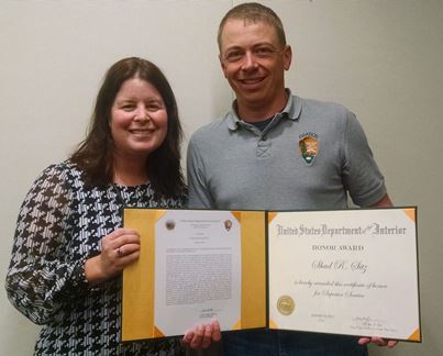 Acting Regional Director Stephanie Burkhart (left) and Shad Sitz (right) hold folder with Superior Service Award.