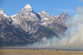 lt= Crews ignite a prescribed fire near the base of the Tetons.