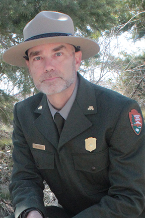 Chad Fisher retirement Chad Fisher in National Park Service uniform in front of pine tree.