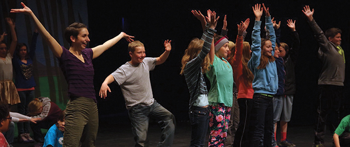 A woman and children raise their hands on a stage.