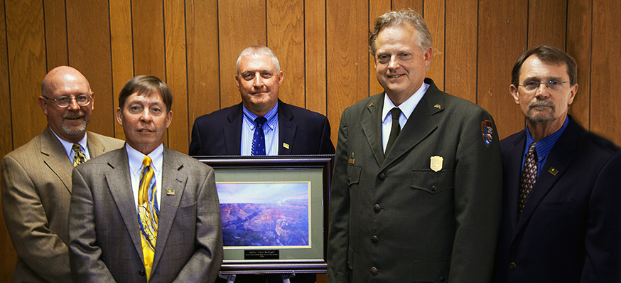 Five men stand with a framed picture of the Grand Canyon.