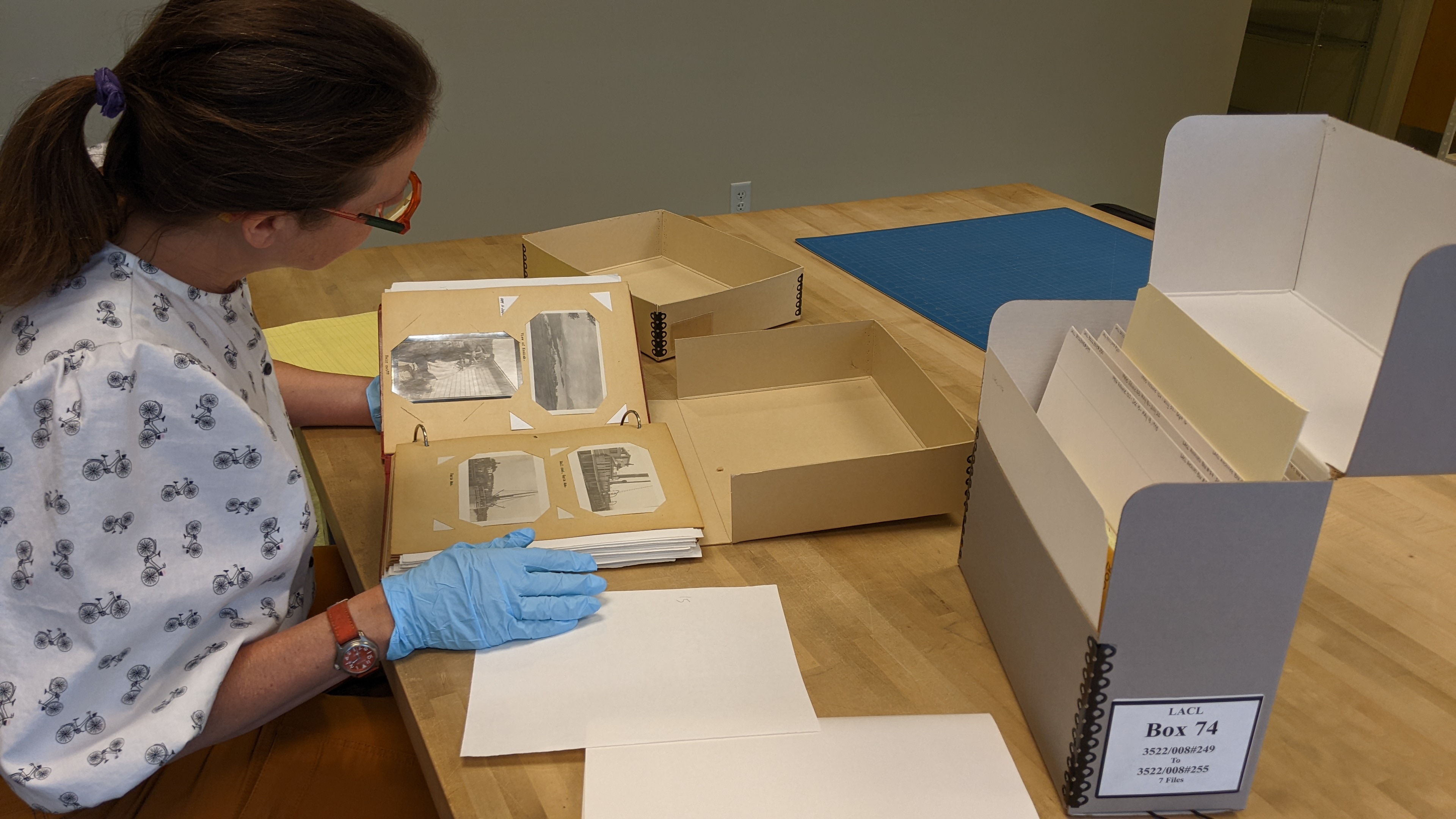 Museum staff reviewing historical photographs. Individual reviewing a historic photograph album from the archives