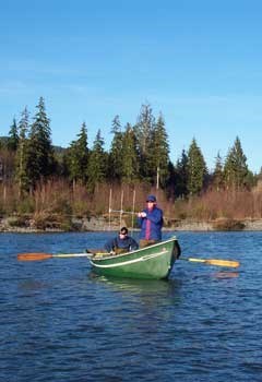 Two researchers on boat, one oaring and one holding an antenna.