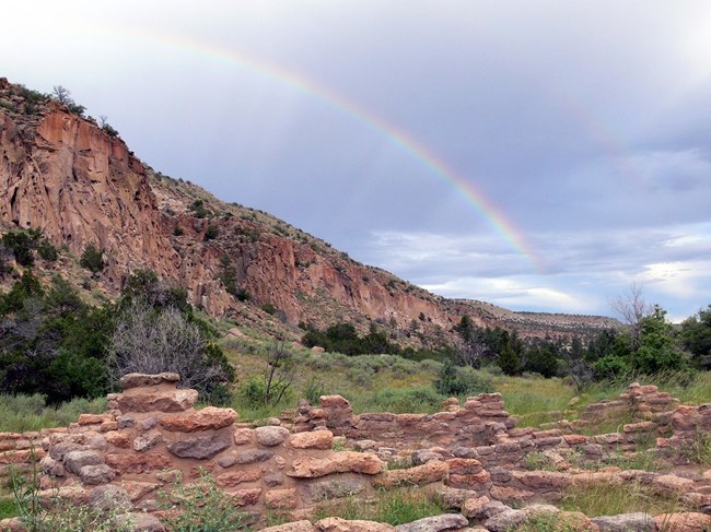 A double rainbow against the sky with the walls of Tyuonyi in the foreground.