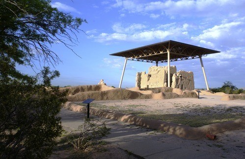 A desert scene with a large clay building covered by a metal awning.