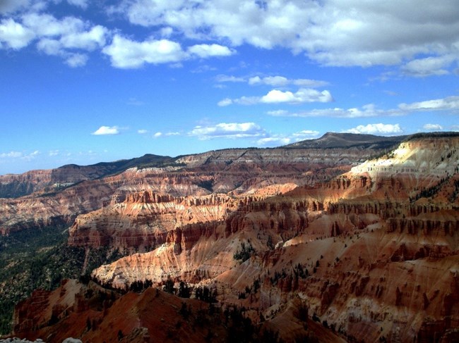 lt= Red rock canyons beneath clouds in a blue sky