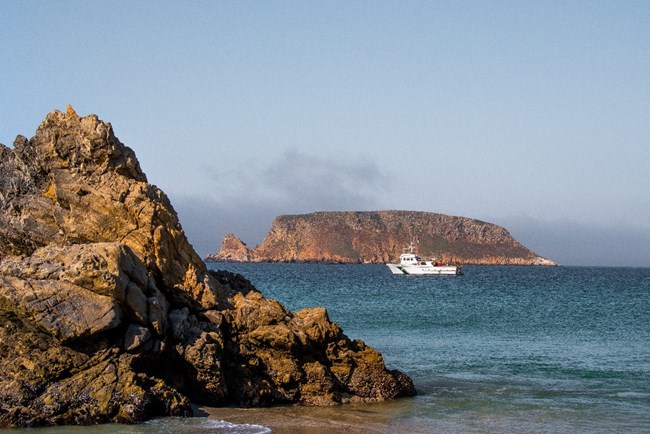 A ranger boat on blue ocean water with a large sharp rock in the foreground.