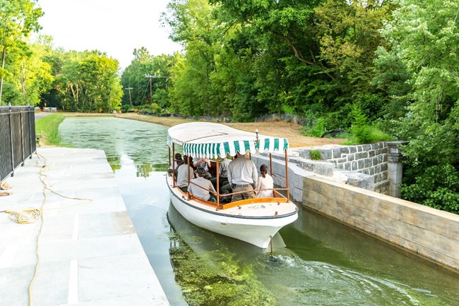 A boat with green and white decoration passes over a watered bridge.