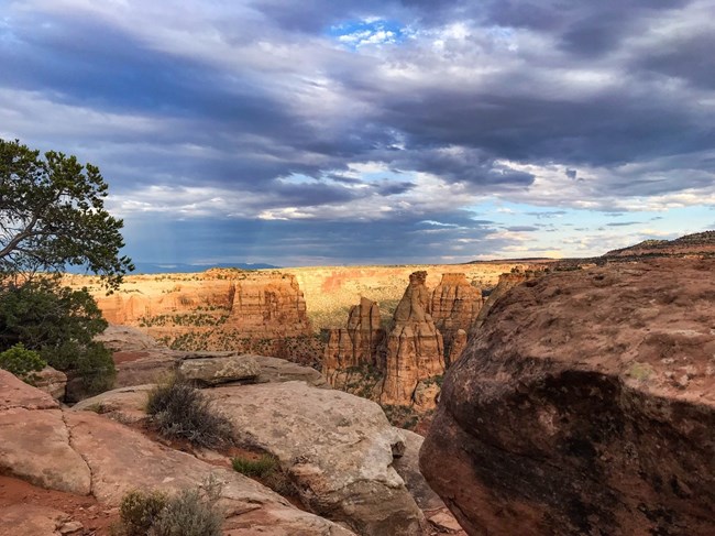 Ledge of red sandstone overlooking a desert canyon under a cloudy sky.