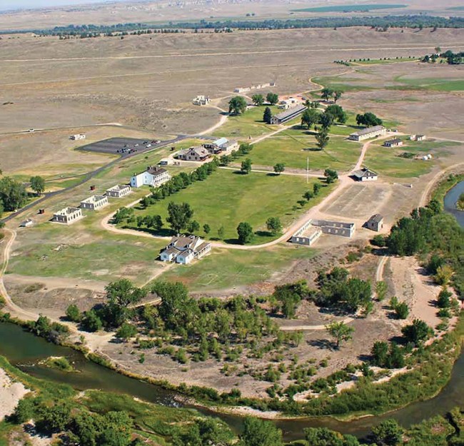 An aerial view of several buildings nestled along the bend of a river in the midst of grasslands.