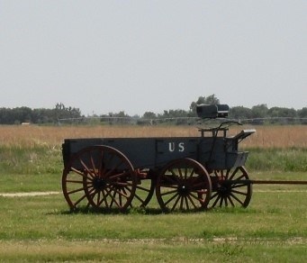 A wooden mail wagon sits in the middle of a field.