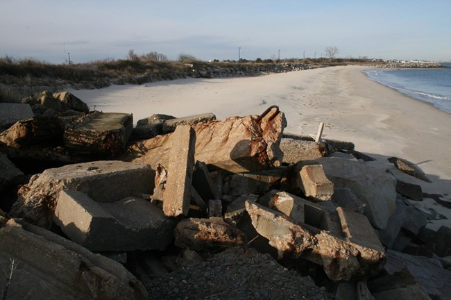 A large pile of stones in the foreground along an expanse of sandy beach.