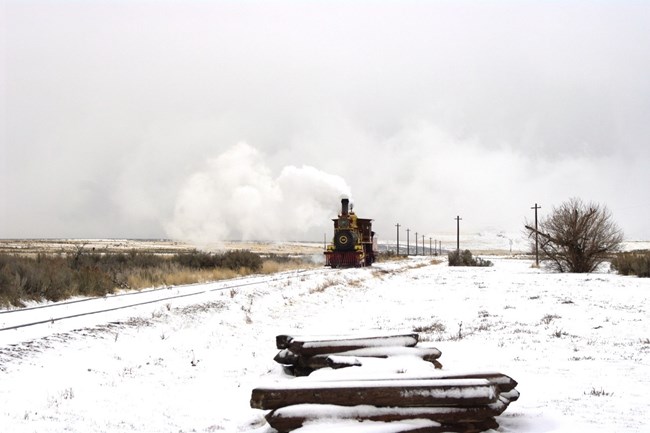A steam train coming down the tracks on a snowy landscape.