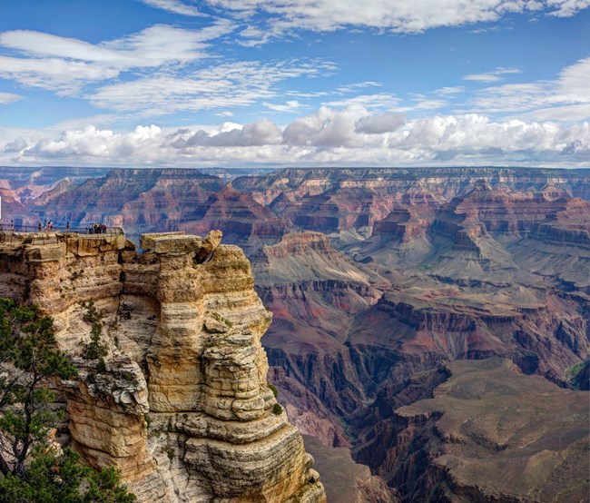 A vast canyon with layered red and brown rock strata underneath a cloudy sky.