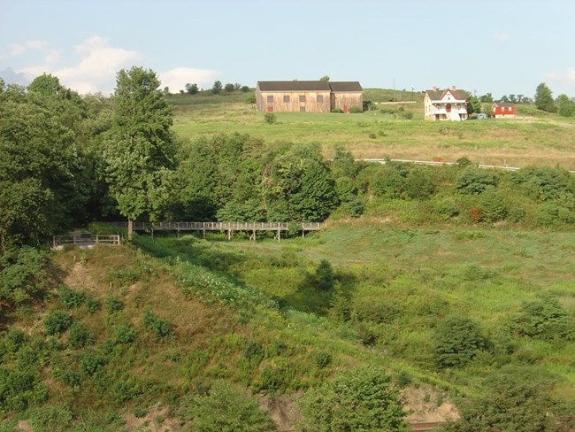 . View of a green field and trees, with three buildings in the background.