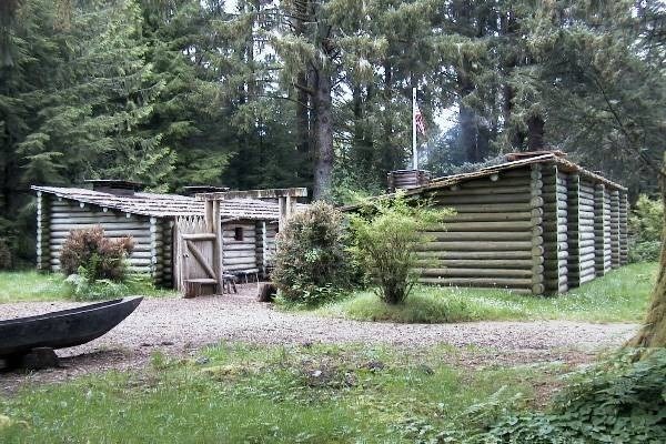 A rocky path leads to two buildings made of logs.  The buildings are backed by tall evergreens.