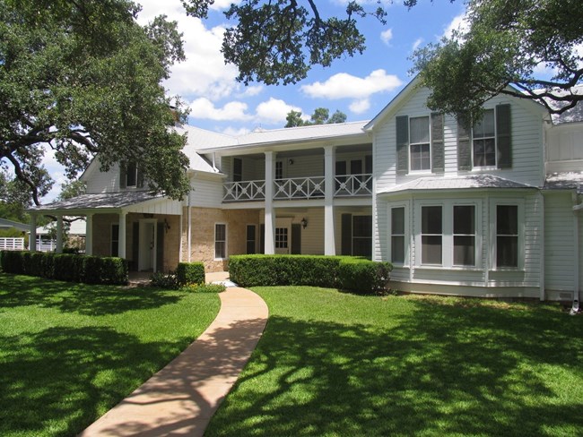 NRCA LYJO A green lawn and walking path in front of a two-story white house.