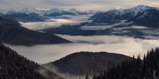 Clouds settle within the peaks of several snow-covered mountains.