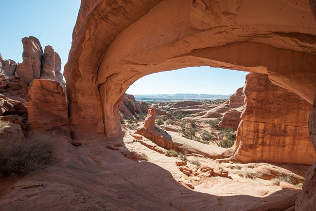 A broad stone arch with rock fins and pinnacles in the distance.