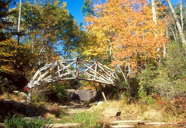 An arched wooden bridge over the South Fork Quantico Creek surrounded by fall foliage.