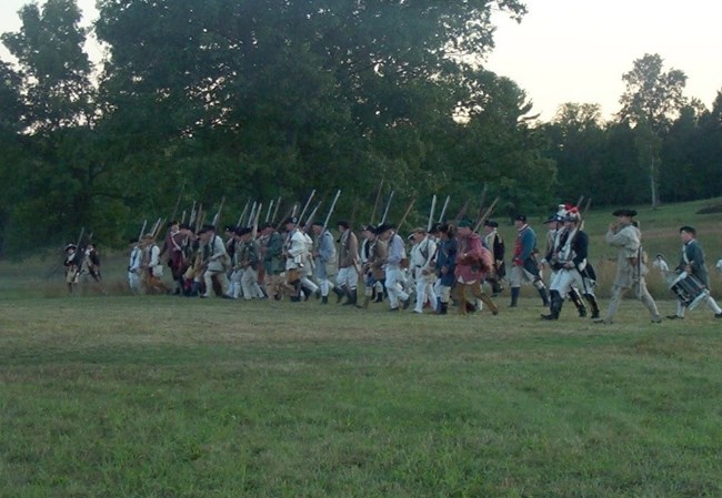 NRCA SARA A line of American soldiers marches across a field at twilight as a light remnant haze of gunsmoke drifts in the air.
