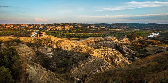 NRCA THRO A rock structure sits on top of a barren butte looking over a lush green river valley bottom.