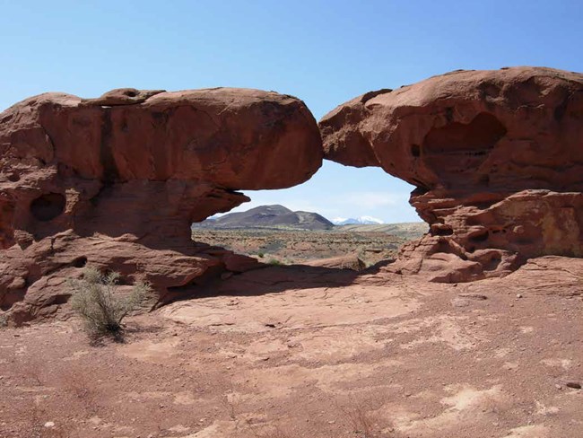 Two large red rocks frame a view of distant prairie landscape and mountains.