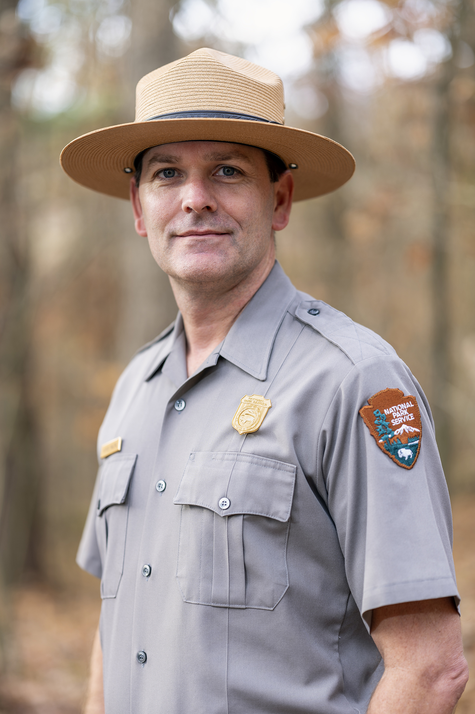 A Caucasian male, dressed in a park ranger uniform, with a brimmed straw hat.