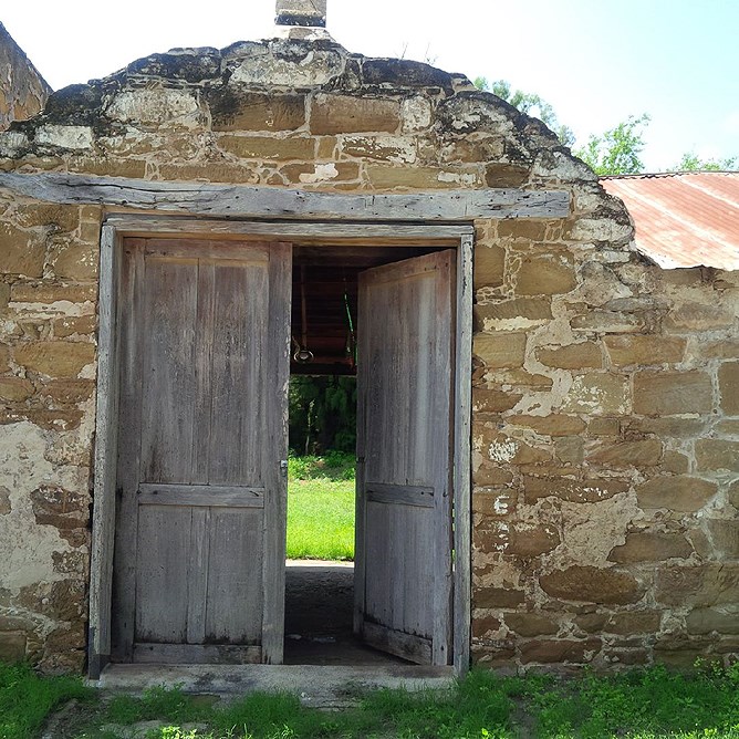 a historic rock structure with wooden doors, grass in front