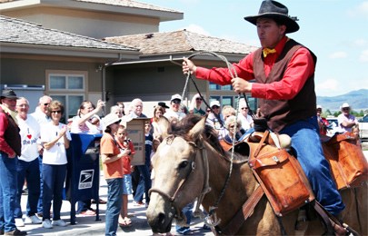 A man on a horse in a red shirt and brown vest rides past a crowd of people.