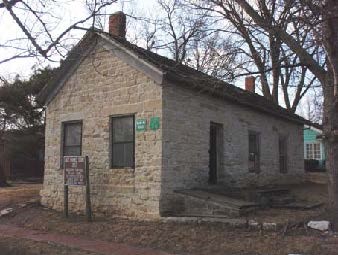 A simple stone building with an angled shingled roof.