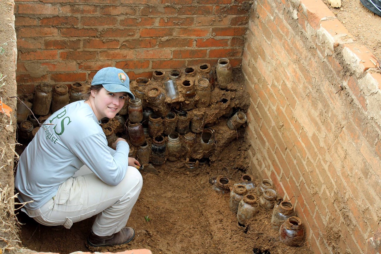 NPS archeologist kneeling next to historic glass jars at Robert E. Howard House Museum in Cross Plains, Texas
