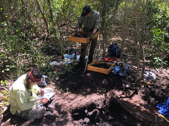 NPS archeologists taking notes and screening soil at an excavation unit