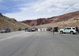 desert road with cars parks everywhere and people crossing road