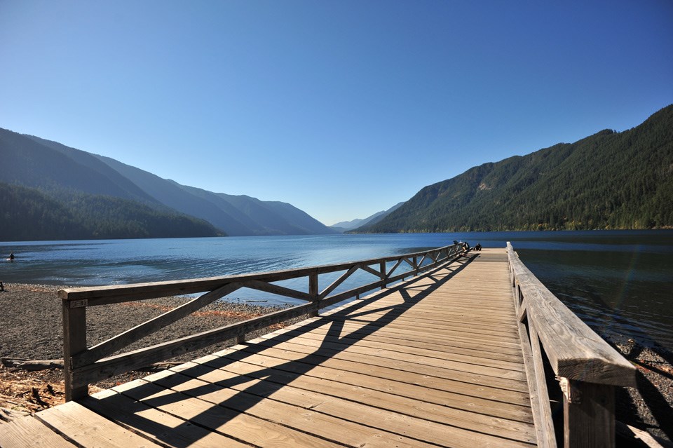 lt= Long wooden dock extends into bright blue water at Lake Crescent Lodge
