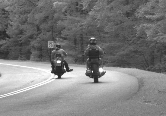 Two motorcyclists travel along a forested roadway in Great Smoky Mountains National Park.