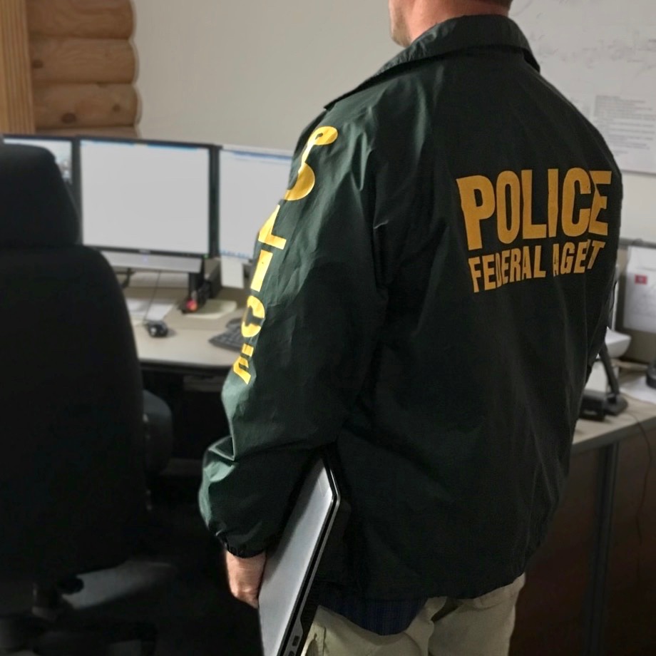 A Special Agent with the NPS Investigative Services Branch holds a laptop computer. In the background are additional computer monitors and pieces of equipment. NPS photo.