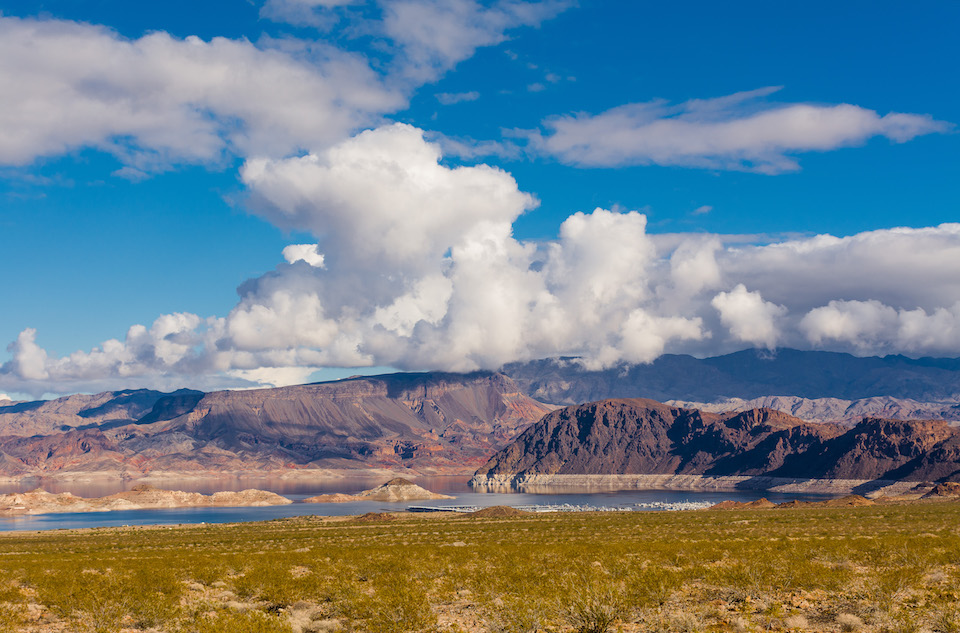 A Special Agent of the NPS Investigative Services Branch worked with US Park Rangers during the investigation and successful prosecution of a man who fired multiple shots at marina guards. White clouds hang in a blue sky above Boulder Basin in Lake Mead National Recreation Area, with a desert landscape in the foreground and the lake and marinas in the distance. NPS photo by A Cattoir.