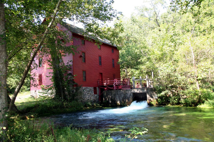 Alley Mill in Ozark National Scenic Riverways is an historic, 3-story red structure with a stone foundation next to a flowing creek and stone millwork. NPS file photo.