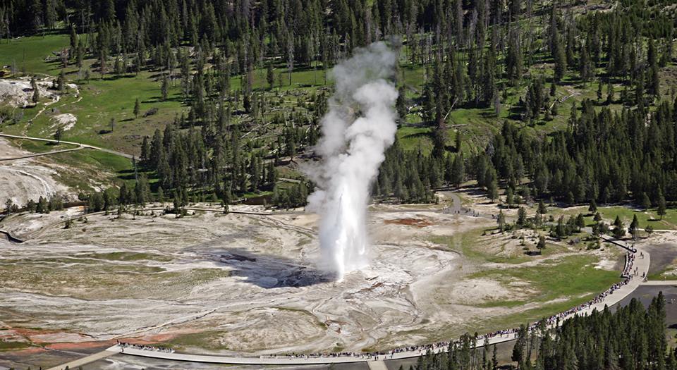 An aerial view of the Old Faithful area of Yellowstone National Park, with people observing the geyser's eruption from a boardwalk. NPS photo.