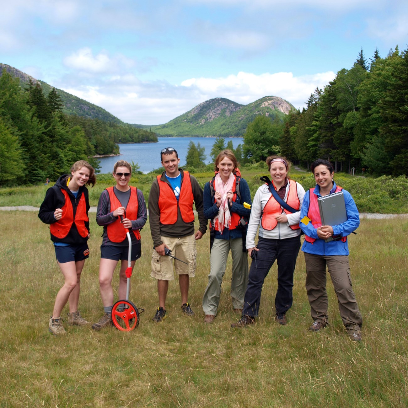 Interns during field trip to Acadia, posing in safety vests and work gear in front of Jordan Pond.