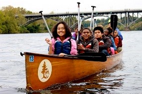 Several youth paddle down a river in a canoe.