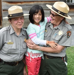 Two rangers smile with a young girl during an event.