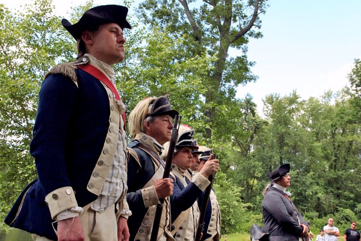 Men in 18th century garb stand in formation for an event.
