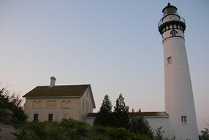 White lighthouse surrounded by trees extends into the sky.